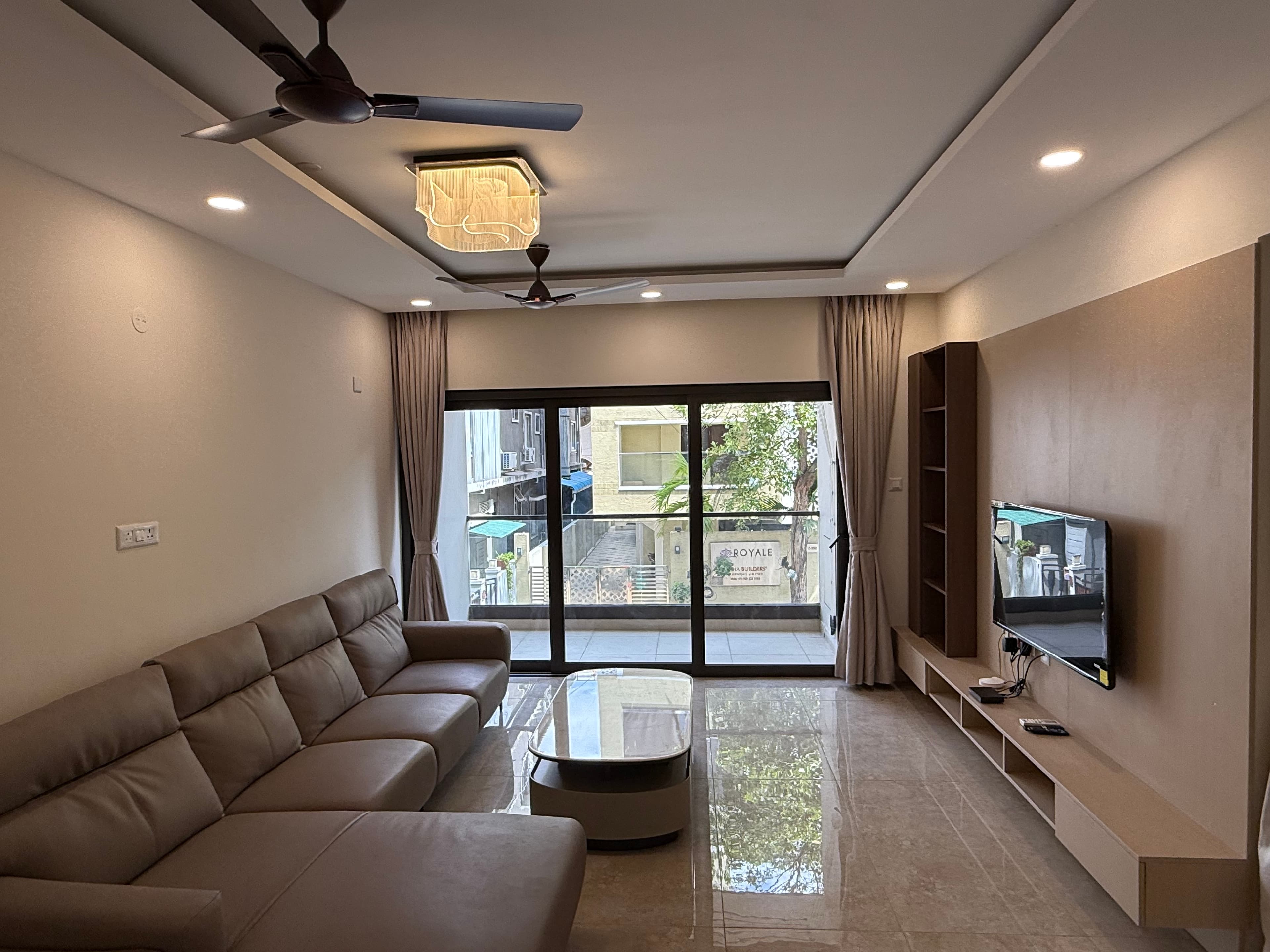 The furnished living hall at Z Block, with the wall-mounted television and seating by the balcony